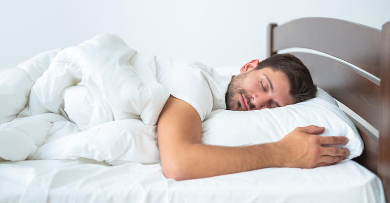 Un homme dorme paisiblement sur un lit blanc dans une ambiance calme et reposante. 