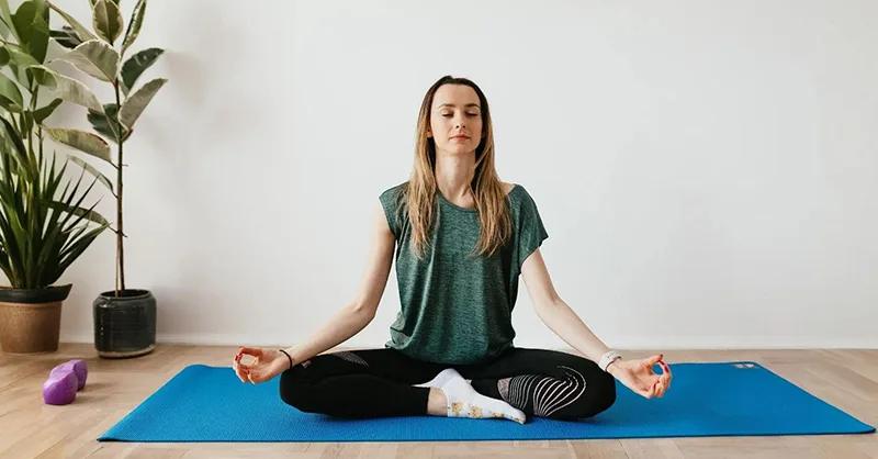 Prévenir le burn-out : image d'une personne, une femme faisant du Yoga ou de la méditation dans une salle à ambiance relaxante.