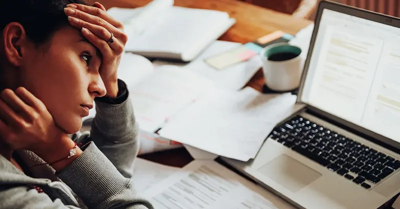 Image d'une  personne, une femme fatiguée la tête entre les mains , assise dans son bureau, regarde l'écran de  l'ordinateur.