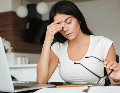 Image d'une personne, une femme travaillant fatigué dans son bureau, avec un ordinateur portable ou laptop, un crayon, des lunettes, un cahier.