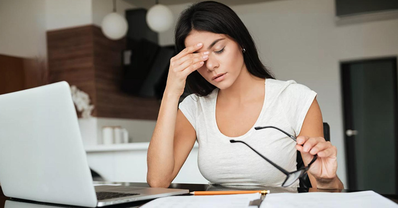 Image d'une personne, une femme travaillant fatigué dans son bureau, avec un ordinateur portable ou laptop, un crayon, des lunettes, un cahier.